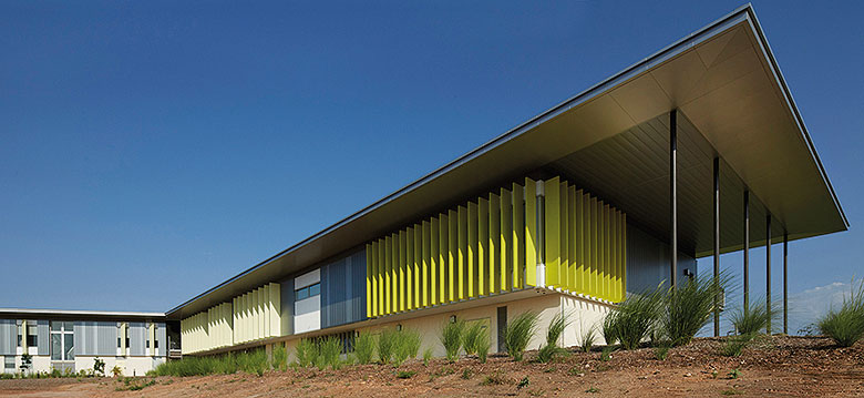 Cantilevered roofs sitting lantern-like atop the weightiness of a concrete block work-base, MacKillop Catholic College in the Northern Territory, roofing, wall cladding, soffits and flashing made from COLORBOND® steel in the colours Windspray®, Jasper®, and Shale Grey™